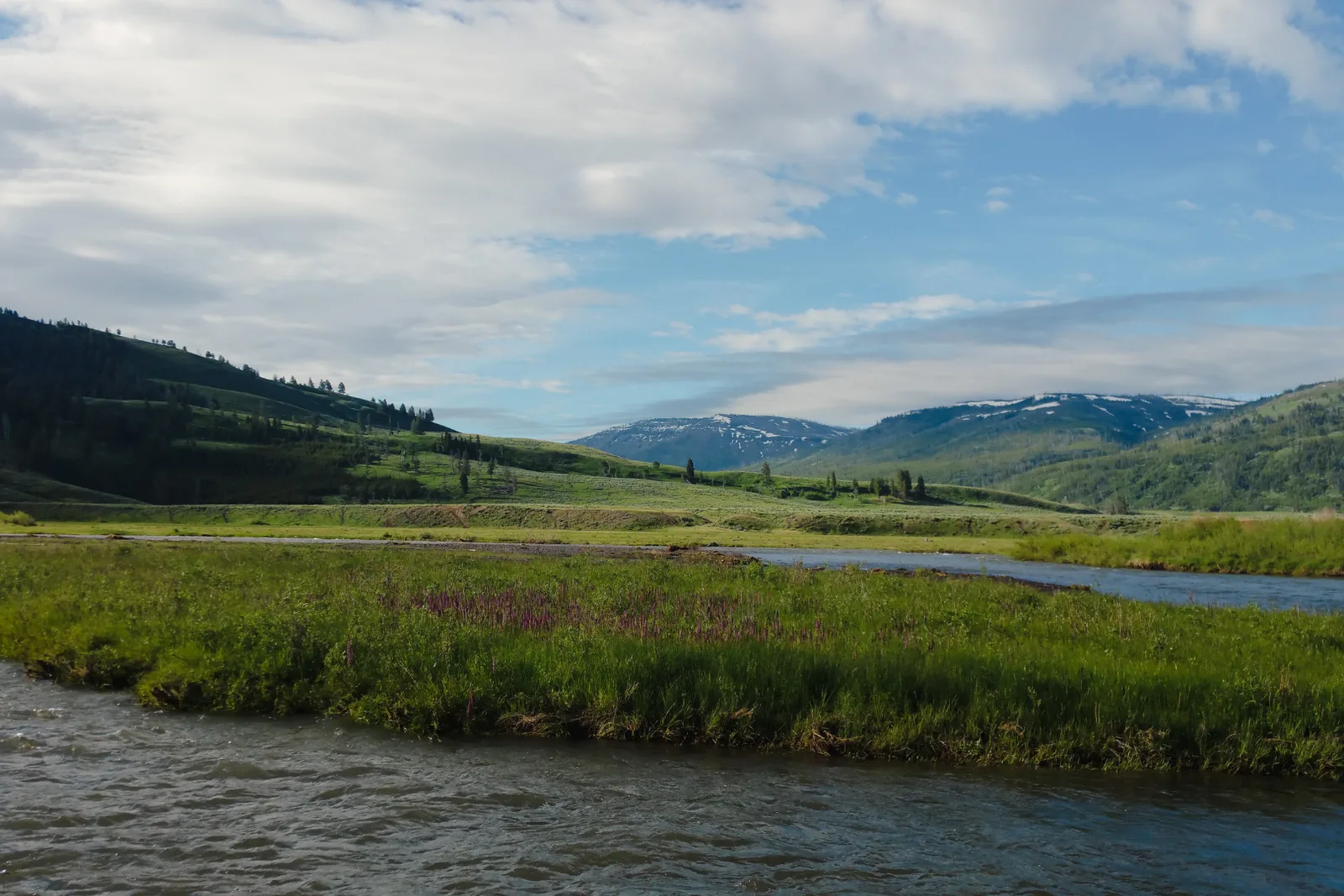 A wide river winding through a green valley below snow-streaked peaks.
