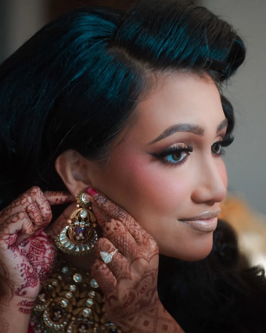 Bridal portrait: a bride in gold jewellery and henna, adjusting an earring.